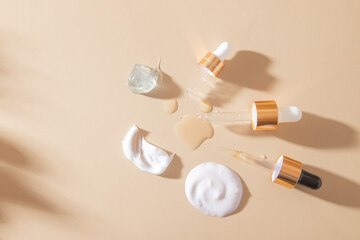 Smears and drops of various cosmetic products top view and pipettes on beige background with shadows