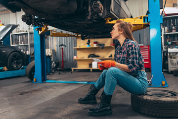 Fototapeta na wymiar Portrait of beautiful young red-headed girl, auto mechanic at auto service station using different work tools for car examining. Gender equality. Work, occupation, car