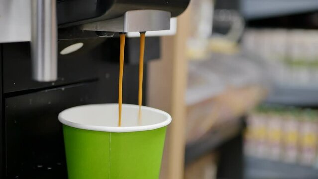 two brown jets of fragrant cappuccino are poured into a green paper cup in a coffee maker