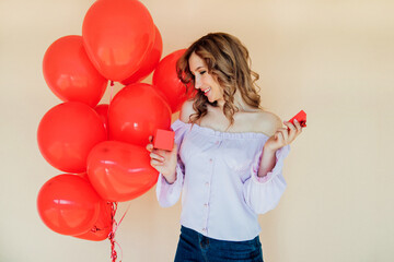 A young woman with heart-shaped balloons and a gift box. The concept of the holiday on March 8 and Valentine's Day.