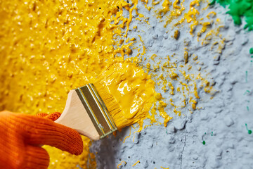 brush in hand paints the wall yellow paint