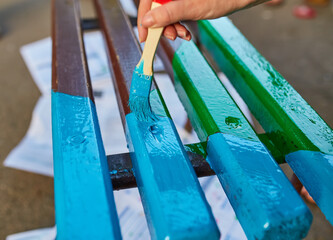 brush in hand paints a bench in bright colors, painting a garden bench