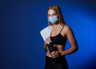 Athletic woman with face mask relaxing after working out in a gym during coronavirus epidemic.