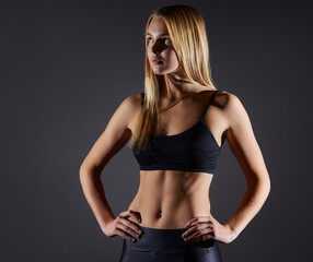 Sportive blonde girl on the background of the black wall of the gym.