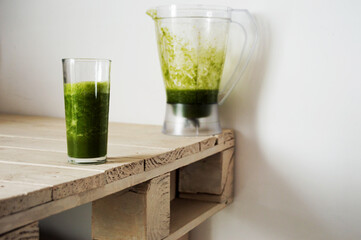 Glass and pitcher with green juice on a slightly grimy white table
