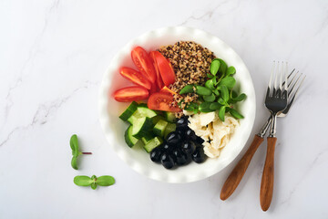 Healthy vegetable lunch from the Buddha bowl with with tomato, cucumber, mozzarella cheese, quinoa, olives and microgreens. Vegan salad buddha bowl. Healthy and balanced food concept.