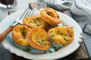Egg muffins with green onions, bacon, cheese and tomatoes on white plate on light background. Healthy high protein and low carb breakfast, ready to eat.