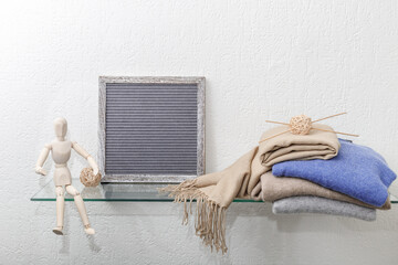Soft sweaters stack of beige, grey, violet and scarf from luxury natural cashmere  lying on glass shelf with wooden manikin and empty vintage  frame