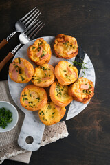 Delicious egg muffins with green onions, bacon, cheese and tomatoes on wooden board on old wooden rustic background. Healthy high protein and low carb breakfast. Homemade food.
