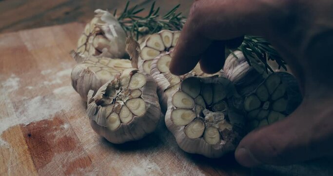 Sliced garlic and a sprig of rosemary on a board in bright light. A man hand puts another head of garlic. Preparing appetizers. Still life with rotation
