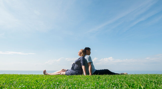 Asian man with a pregnant woman are resting in nature in a picturesque place, sit on the green grass