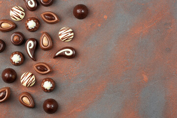 Chocolate pralines assortment on brown background, flat lay, top view with copy space	