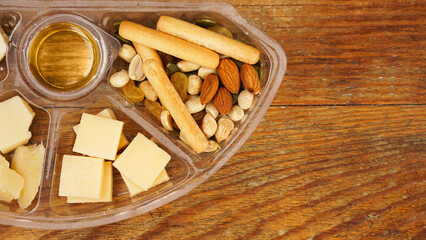 Set of food in a plastic container. Cheese plate for a picnic on a wooden background. Various cheeses, nuts and honey