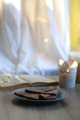 Plate of chocolate, open book, reading glasses, lit candle and flowers on the table. Selective focus.