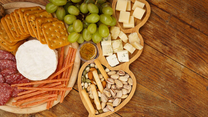 Different tasty appetizers on wooden background, top view. Snacks for wine. Cheese and meat plate. Sausages, cheese, nuts, grapes, crackers