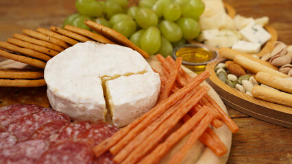 Different tasty appetizers on wooden background. Cheese and meat plate. Sausages, cheese, nuts, grapes, crackers. Focus on Camembert cheese