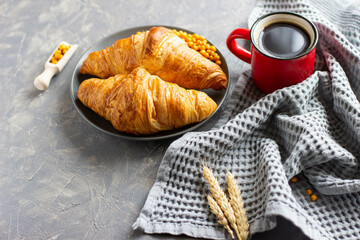 two croissants on a grey plate and a red coffee mug stand on a grey background