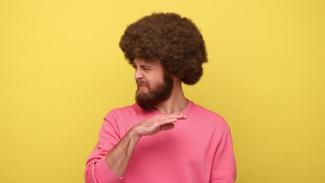 Man with Afro hairstyle holding breath with fingers on nose, grimacing in disgust, expressing repulsion to stink, fart gases, wearing pink sweatshirt. Indoor studio shot isolated on yellow background.