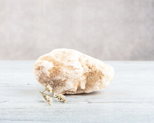 Stone podium and sprig of a white flower on a white wooden background, front view, copy space. Empty showcase for product presentation.