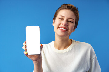Portrait of a young woman showing blank screen mobile phone while standing over blue background