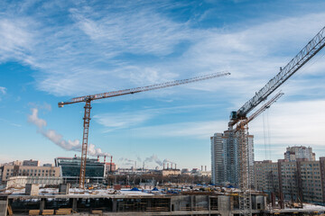 Fototapeta na wymiar Construction cranes at a construction site in the city against the blue sky in winter conditions. Construction of a new building. The concept of building a new area.