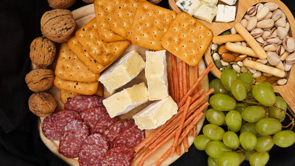 Cheese platter with assorted cheeses, grapes, nuts over black background. Italian cheese platter for wine.