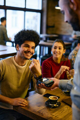 Happy man using smart watch while making contactless payment to waiter in a pub.