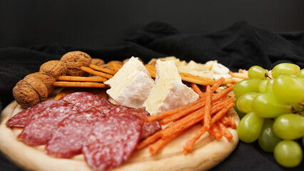 Cheese platter with assorted cheeses, grapes, nuts over black background. Italian cheese platter for wine.