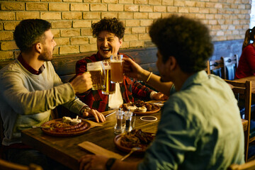 Cheerful group of young men toast with beer while having lunch in a pub.