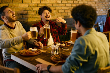 Group of cheerful men have fun and laugh while drinking beer and eating in pub.