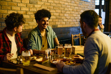 Multiracial group of male friends talk while drinking beer and eating in pub.