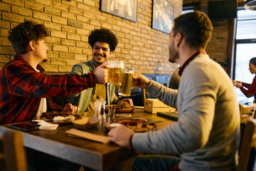 Young happy men toast with beer while having lunch together in a pub.