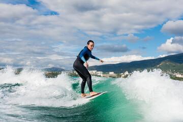 Young athletic female in wetsuit riding on endless waves behind a boat on sunny day. Woman practice wakeboarding, carving behind the baot. Watersport concept.