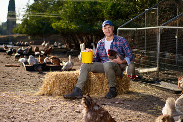 Countryman holding brown chicken in hands in hen house