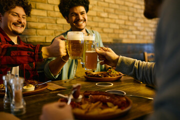 Close-up of cheerful men toast with beer while having lunch in pub.