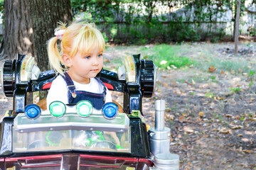 A little girl on a toy car looks away.