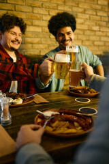 Close-up of happy male friends toast with beer while gathering for lunch in pub.