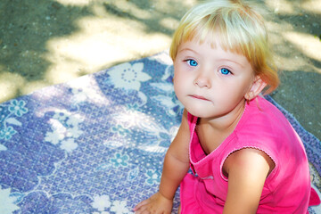 A little girl with beautiful eyes sits on a blanket and looks at the camera.