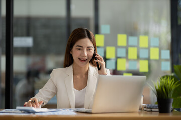 Asian woman talking on the phone, she is a salesperson in a startup company, she is calling customers to sell products and promotions. Concept of selling products through telephone channels.