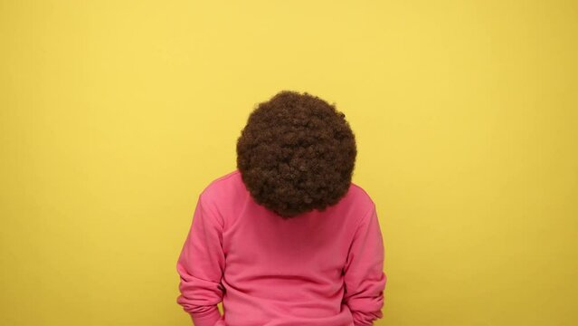 Man with Afro hairstyle touching his head and showing explosion, looking worried and shocked, deadline, professional burnout, wearing pink sweatshirt. Indoor studio shot isolated on yellow background.