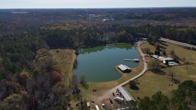 Aerial fly to green odd shaped lake with road and trees barn beside lake