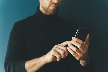 Using a smartphone by a young man on a blank background. Phone in hand while using the Internet, messenger, shopping, communication. Technology, applications, business concept.