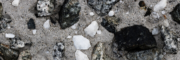 Concrete wall texture with pebbles. Decorative rough concrete surface with white, black and gray stones. Wide panoramic texture for background and design.