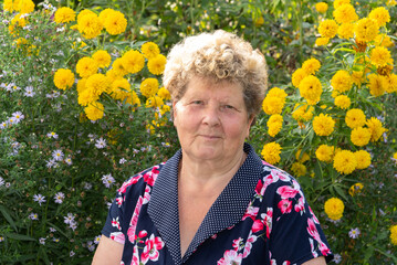 Portrait of woman 60s years old against background of yellow flowers in garden