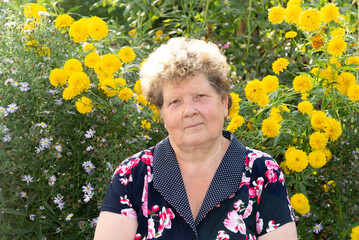 Portrait of woman 60s years old against background of yellow flowers in garden