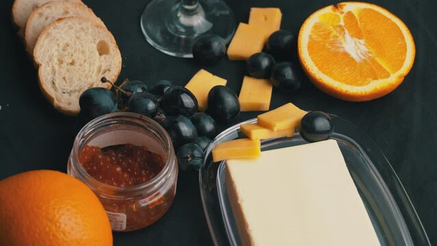 A glass of ros wine swirls with appetizers. Aesthetics of wine with cheese. Alcohol, romance, evening. Cheese, butter, red caviar, grapes, baguette, orange. View from above.