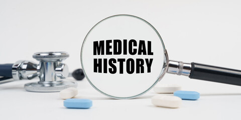 On a white surface lie pills, a stethoscope and a magnifying glass with the inscription - MEDICAL HISTORY