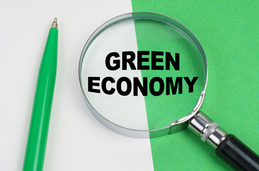 On a white-green background lies a pen and a magnifying glass, inside which is the inscription - Green economy