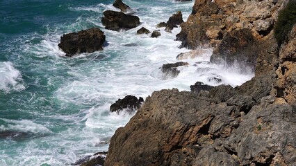 Crystal clear turquoise water, waves crashing on the rocky shore, and the ruins