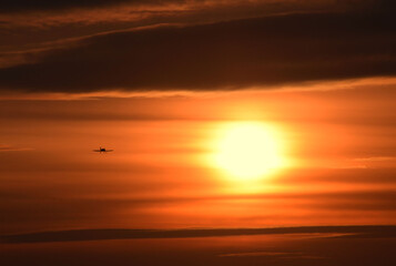Photo of a sunset, depicting a huge sun and a small plane, against the background of the evening sky